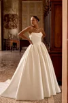 A woman wears the 88436/KELSEY by Justin Alexander—a strapless, full-skirted gown—standing indoors with hands on hips, gazing to the side in an ornate, classic room.
