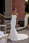 A woman in a strapless white KAI/88439 by Justin Alexander wedding dress stands outdoors near stone steps and a table set for an event.
