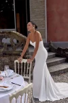 A woman in a strapless white KAI/88439 by Justin Alexander wedding dress stands outdoors near stone steps and a table set for an event.