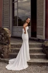 A woman in a strapless white KAI/88439 by Justin Alexander wedding dress stands outdoors near stone steps and a table set for an event.