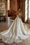 A woman in the KEEGAN/88440 by Justin Alexander poses indoors before ornate wooden doors, wearing a white, floor-length, sleeveless bridal gown with a fitted bodice in an elegant historic setting.