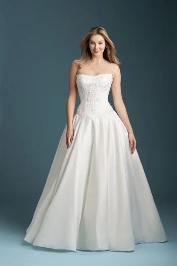 A woman wears the A1350 by Allure strapless white ball gown wedding dress with floral bodice embellishments, standing against a plain blue background.