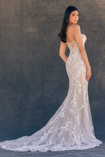 A woman poses against a dark background in the C725 by Allure, a strapless, fitted white lace wedding gown with a long train.