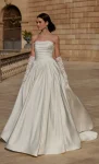 A woman in product 63114, a strapless white ball gown with lace gloves, stands outside on a stone courtyard before a large building.