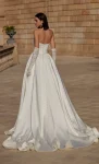 Flares Bridal + Formal | 63114 A woman in product 63114, a strapless white ball gown with lace gloves, stands outside on a stone courtyard before a large building.