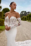 Flares Bridal + Formal | HOPE/88353 by Justin Alexander A woman stands on stone steps before an old building, wearing the HOPE/88353 by Justin Alexander: a strapless, fitted white wedding gown with a sheer lace bodice and long lace train.