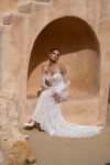 A woman in the white lace CINDY/JC2597 off-the-shoulder wedding dress with long sheer lace sleeves stands before a beige textured background.