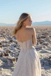 A woman poses before a rocky backdrop in the JULIETTE/F380 by Allure, a strapless lace wedding gown featuring a thigh-high slit and sheer bodice accents.