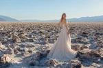 A woman poses before a rocky backdrop in the JULIETTE/F380 by Allure, a strapless lace wedding gown featuring a thigh-high slit and sheer bodice accents.