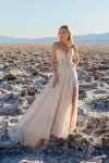 A woman poses before a rocky backdrop in the JULIETTE/F380 by Allure, a strapless lace wedding gown featuring a thigh-high slit and sheer bodice accents.