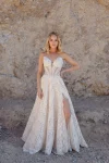 A woman poses before a rocky backdrop in the JULIETTE/F380 by Allure, a strapless lace wedding gown featuring a thigh-high slit and sheer bodice accents.