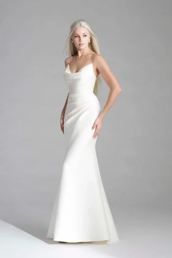 Woman wearing the ERIN/MJ1153 by Allure, a fitted, floor-length white gown with a draped neckline, stands against a plain light gray background.