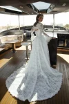 Wearing VENICE, a long-sleeved lace wedding dress, a woman stands on the deck of a modern yacht.