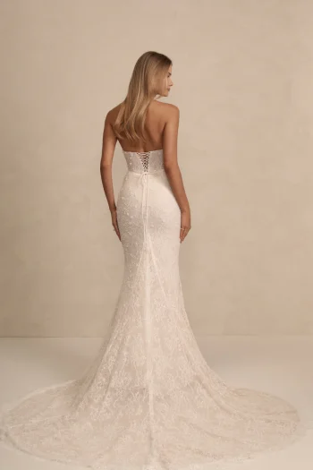 A woman faces away, wearing the HAVEN by Made with Love—a strapless, lace ivory wedding gown featuring a fitted bodice, corset back, and long train.