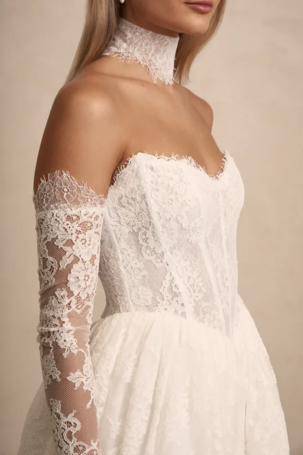 Woman shown from the side wearing the PRIM by Made with Love off-shoulder white lace wedding dress with matching lace gloves and choker.