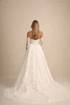 A woman in the strapless PRIM wedding dress by Made with Love stands outdoors in a courtyard, surrounded by greenery and elegant stone structures.