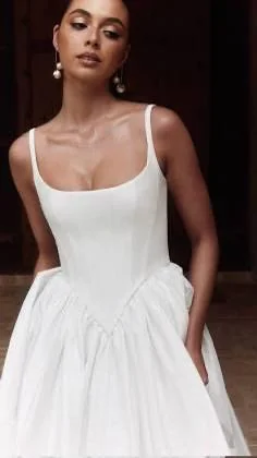 Woman wearing the PROTEA by Alena Lenna white sleeveless dress with a fitted bodice and full skirt, hands in pockets—a chic look radiating effortless elegance.