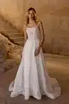 Woman in a strapless white lace wedding gown stands indoors near stone stairs and a textured wall.