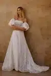 Woman in a strapless white lace wedding gown stands indoors near stone stairs and a textured wall.