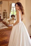 A woman wearing the 88504/MCKENNA wedding gown by Justin Alexander stands in an elegant room with wooden floors, arched doorways, and classic furnishings.