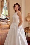 A woman wearing the 88504/MCKENNA wedding gown by Justin Alexander stands in an elegant room with wooden floors, arched doorways, and classic furnishings.