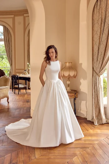 A woman wearing the 88504/MCKENNA wedding gown by Justin Alexander stands in an elegant room with wooden floors, arched doorways, and classic furnishings.