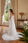 A woman wearing the 88511/MELODY by Justin Alexander, a strapless white wedding gown, stands indoors beside large potted plants. Natural light and classic decor provide an elegant and timeless backdrop for this exquisite dress.