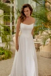 A woman wearing the 88511/MELODY by Justin Alexander, a strapless white wedding gown, stands indoors beside large potted plants. Natural light and classic decor provide an elegant and timeless backdrop for this exquisite dress.