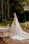 Wearing the 88519/MARA by Justin Alexander, a woman stands indoors near an open door, adjusting her hair in a strapless white wedding gown with a garden visible outside.