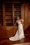 Woman in a strapless white lace and satin gown stands by wooden bookshelves, looking to the side.