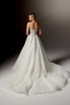 A woman stands gracefully against a neutral background, wearing the 99405/RAVENNA strapless white wedding gown by Justin Alexander, featuring delicate floral patterns and paired with a long sheer veil.
