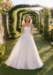 Wearing the A1402 by Allure, a woman stands on a garden path beneath green archways, looking to the side in natural sunlight.