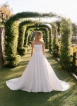 Wearing the A1402 by Allure, a woman stands on a garden path beneath green archways, looking to the side in natural sunlight.