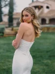 A woman exudes allure in the A1488 by Allure, a strapless white dress, as she stands on grass before a stone building with arched windows and a tiled roof.