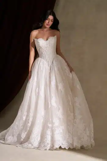 Woman wearing the C845 by Allure strapless, lace-embroidered ball gown wedding dress, standing against a neutral background with a dark drape.