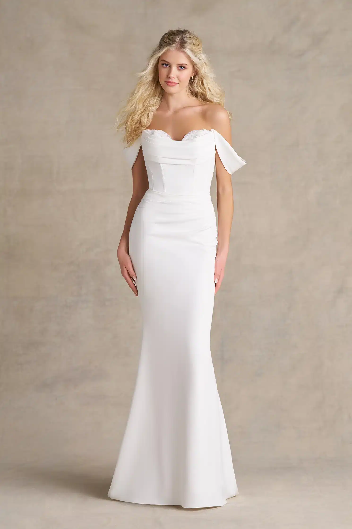 A woman stands against a neutral background wearing the R3989 by Allure, an off-the-shoulder, fitted white bridal gown featuring a subtle mermaid silhouette that exudes elegance. A woman stands against a neutral background wearing the R3989 by Allure, an off-the-shoulder, fitted white bridal gown featuring a subtle mermaid silhouette that exudes elegance.