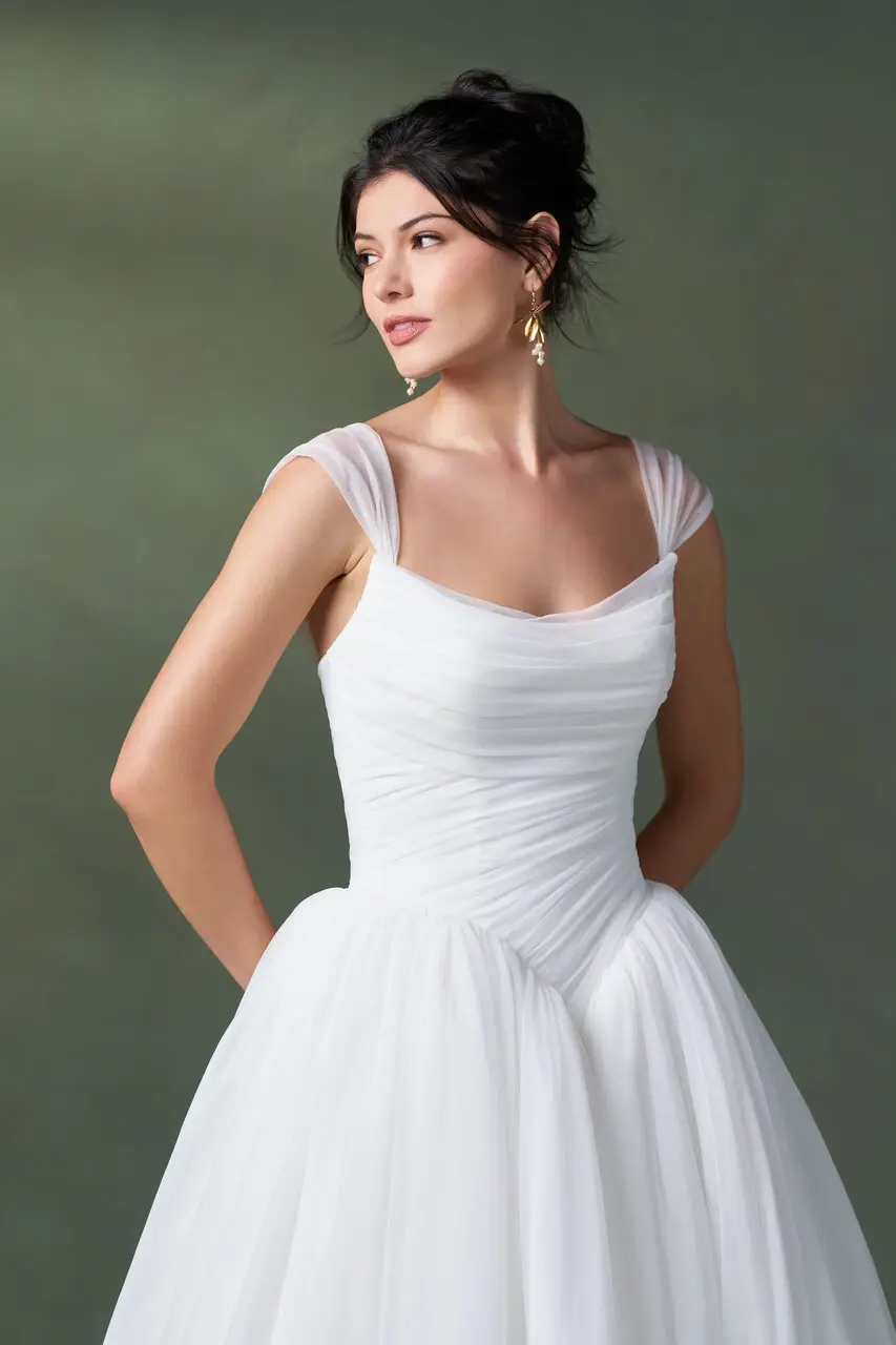 Woman wearing an A1500 by Allure white, floor-length wedding dress with a ruched bodice and cap sleeves. Woman wearing an A1500 by Allure white, floor-length wedding dress with a ruched bodice and cap sleeves.