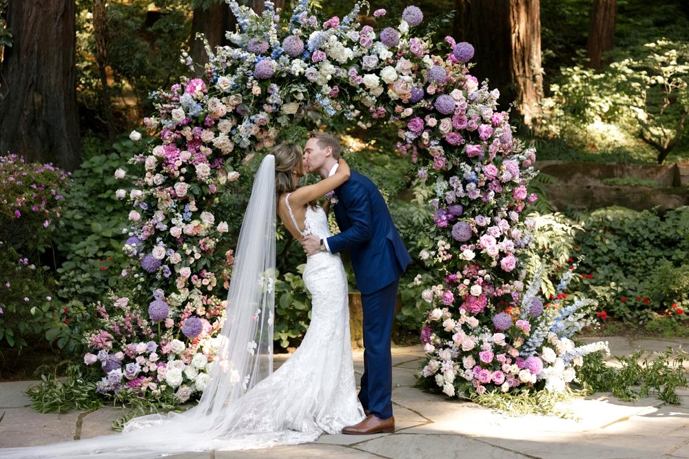 A bride in a mermaid wedding dress with a train at an outdoor ceremony